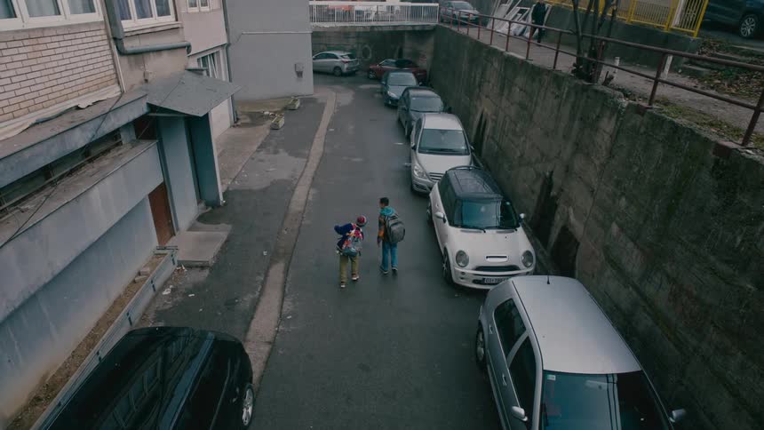 Two children walk down an alley filled with parked cars