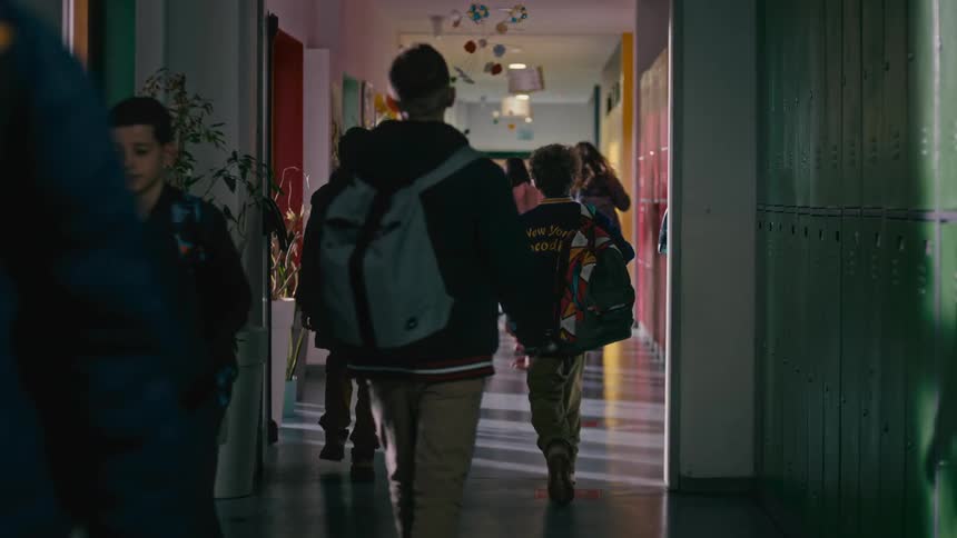 A young boy closes his school locker and walks down a hallway filled with other students