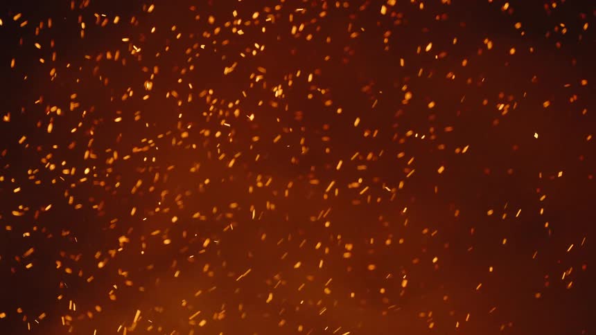 Countless embers and some smoke rise up into the air from a fire below