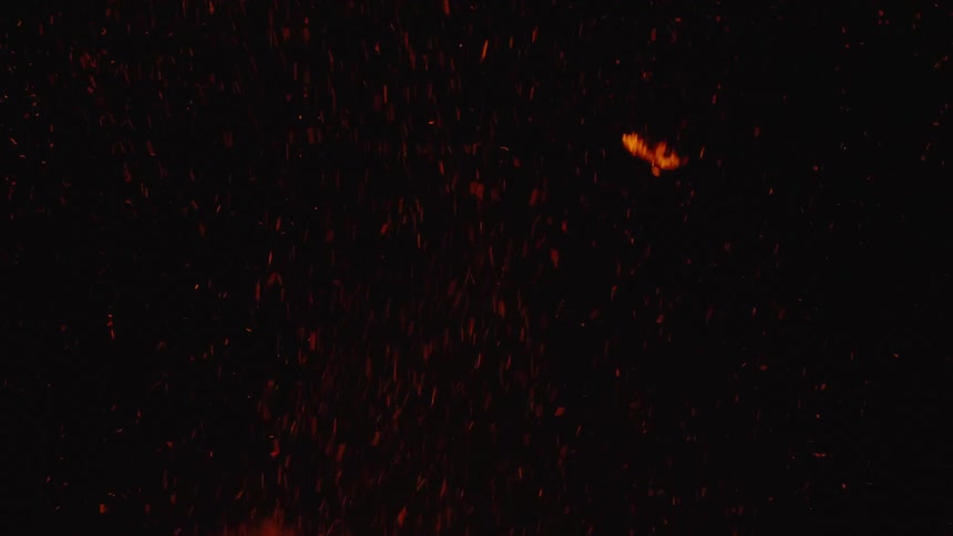 Ash and sparks rise from rapidly burning fire at night