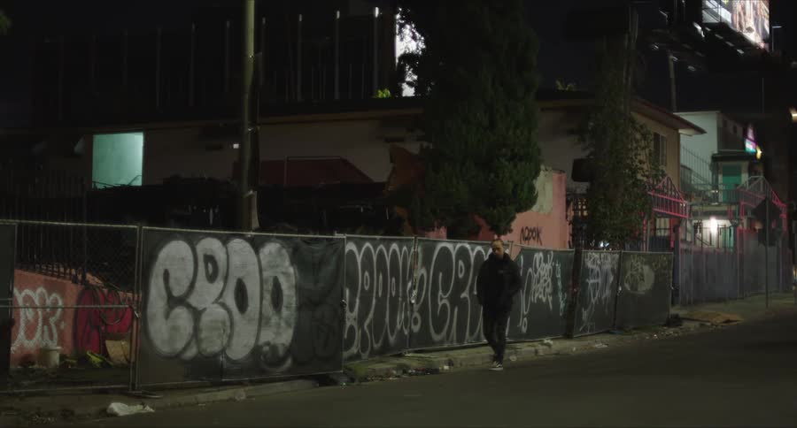 Man walking along a city street with graffiticovered walls at night