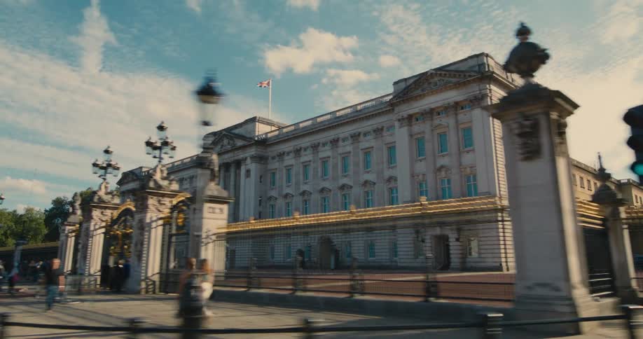 Buckingham palace and its gates under a bright sky with pedestrians nearby