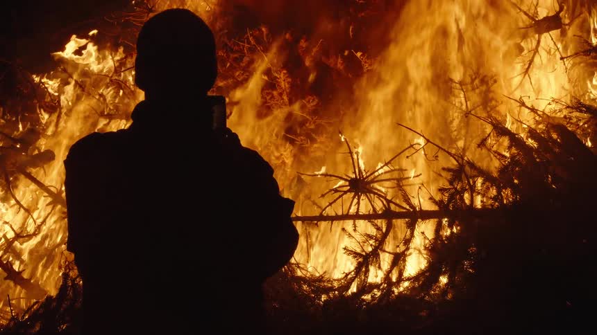 Man with his back and front to a forest on fire at night
