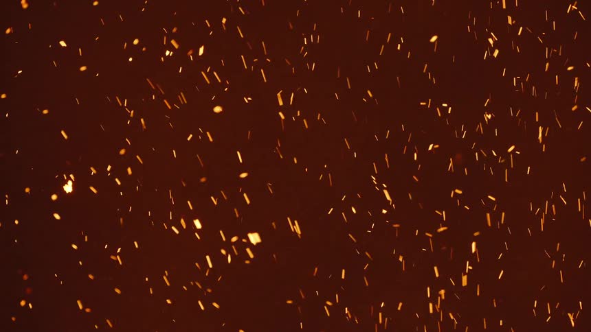 Glowing embers move as they rise in the smoke of a fire