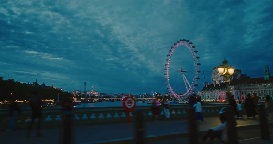 Pedestrians walk across westminster bridge with the london eye in the background at night