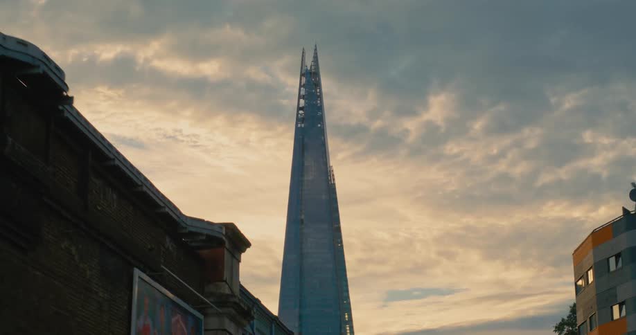 Skyscraper with an elongated pyramidal shape towers over other buildings on a cloudy day