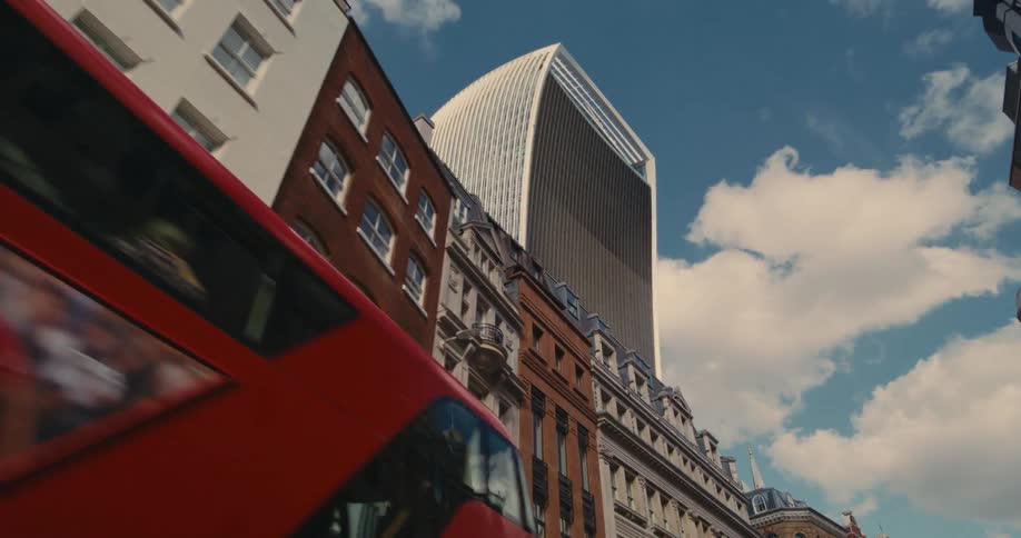A huge office building with many windows in a city and there is a red bus parked on the street