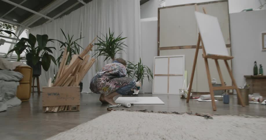 A woman shakes paint of a container and on to a canvas
