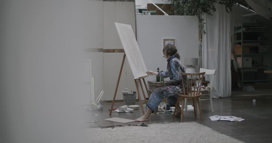 Woman sitting in a chair painting a picture on a bench