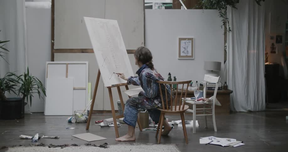 A woman painting a canvas sitting in a studio during the day