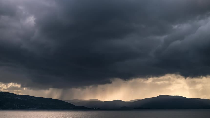 Gray and dark clouds float over mountains and the sea