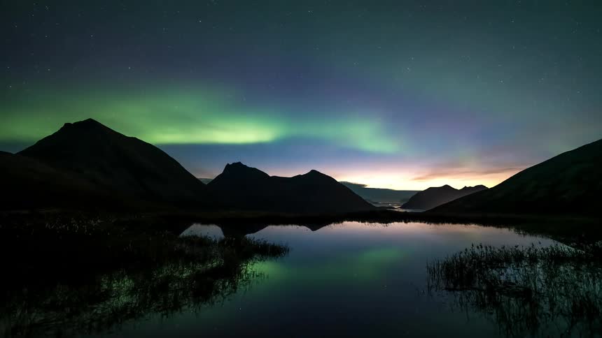 The aurora borealis in the sky reflecting in a lake in the middle of mountains