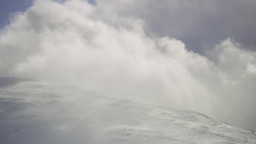 A huge white cloud passing quickly to the left next to a snowcovered peak on the ground