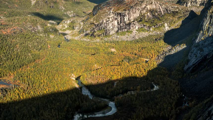 A river that runs through a forest in a region with many rocky mountains and dense clouds in the sky