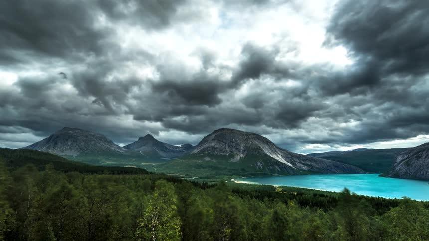 Timelapse landscape of mountain ranges with blue water and forest with clouds passing by