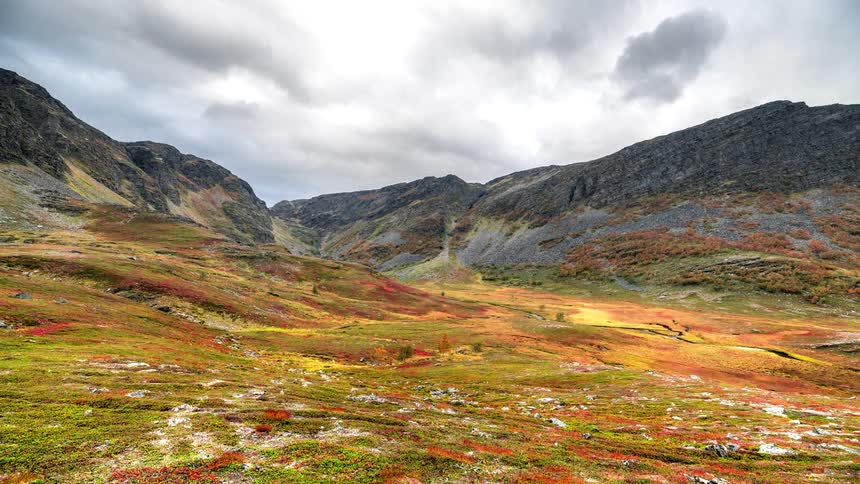 Mountains and a colorful valley with vegetation under a cloudy sky