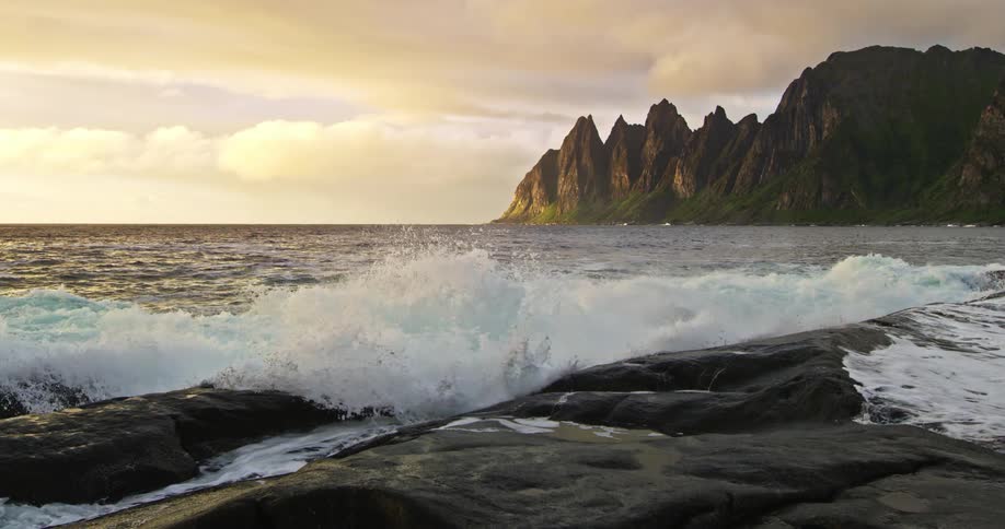 Waves break on a beach with mountains during sunset