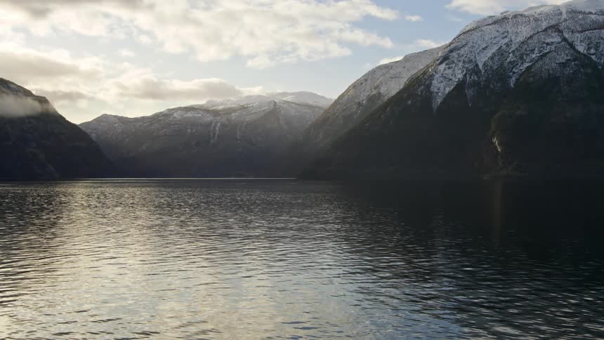 A river with small ripples in a mountainous region with the tops of mountains covered in snow