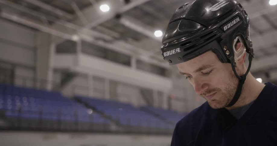 A hockey player wearing a helmet looks down in an arena