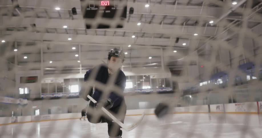 A man at a hockey rink hitting a puck into the goal