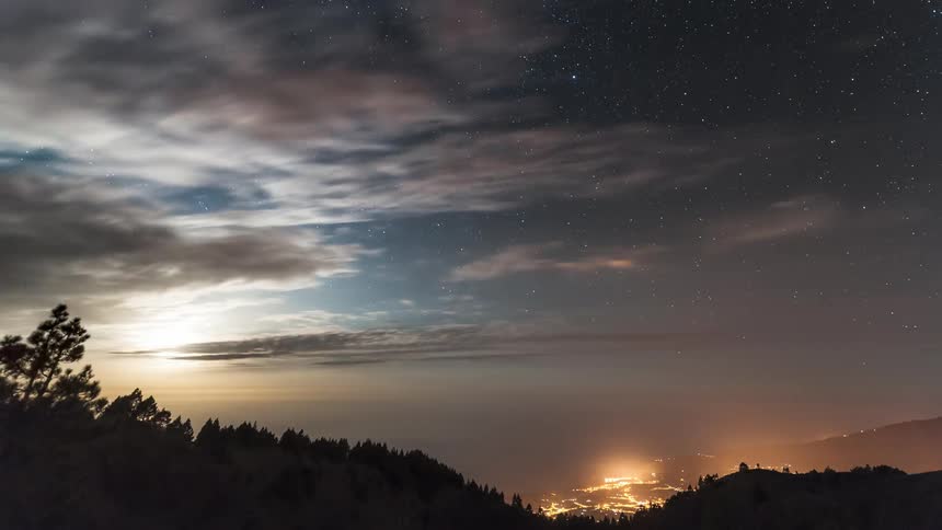 Landscape of mountains with forests and in the background a city with clouds passing by in time lapse of the day getting dark