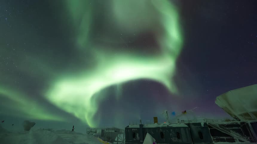 green beams in the sky of Aurora Australis on top of an observatory full of equipment and flags