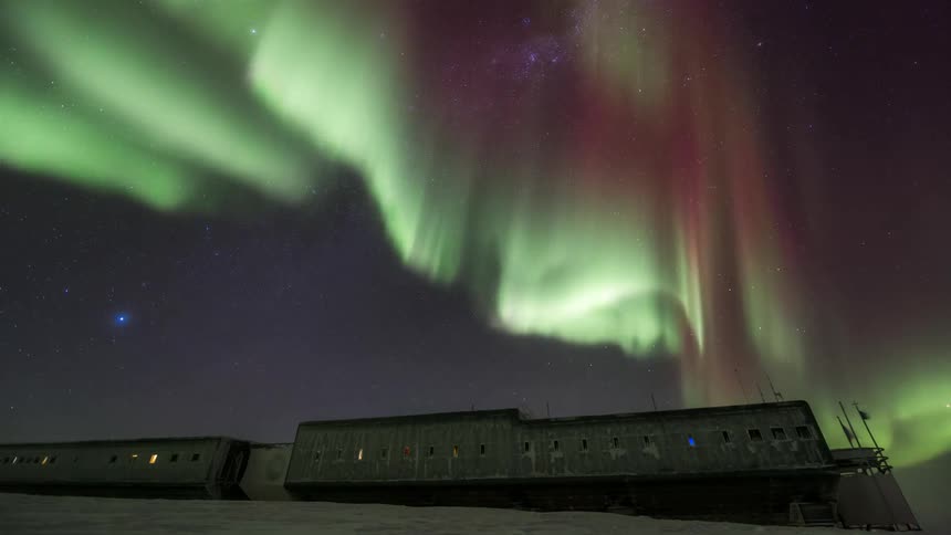 A research station illuminated by Aurora Australis in the starry sky