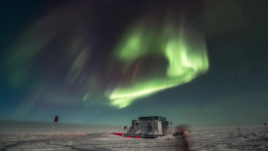 A bright green Aurora Australis above a research station in the middle of the snow
