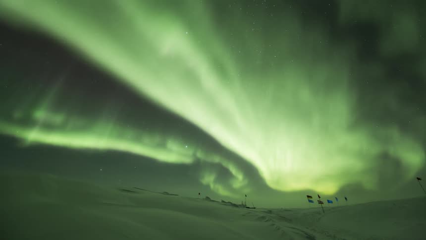 The Aurora Australis with a green glow over the south pole and several flags