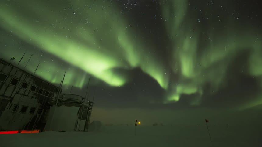 Research center in a polar location with the night sky in timelapse passing the Aurora Australis