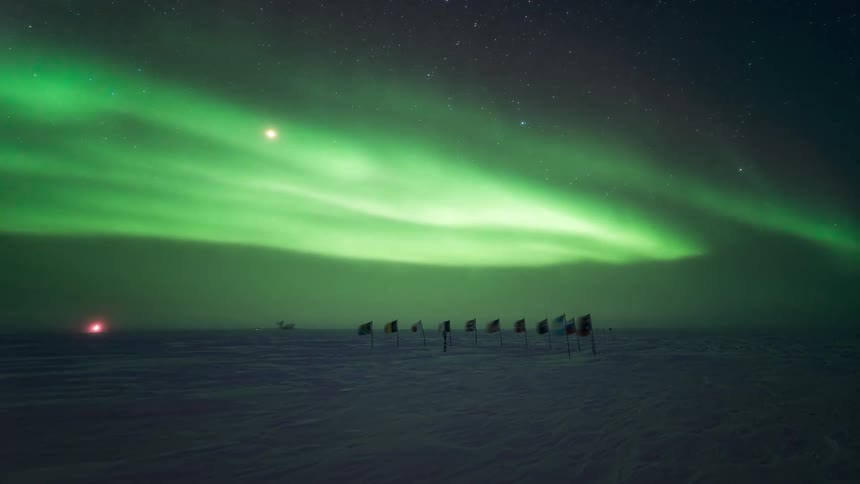 A row of flags are in the snow with Aurora Australis