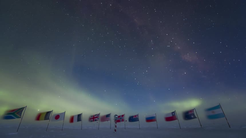 Aurora Australis floats through night sky above multiple national flags posted near south pole
