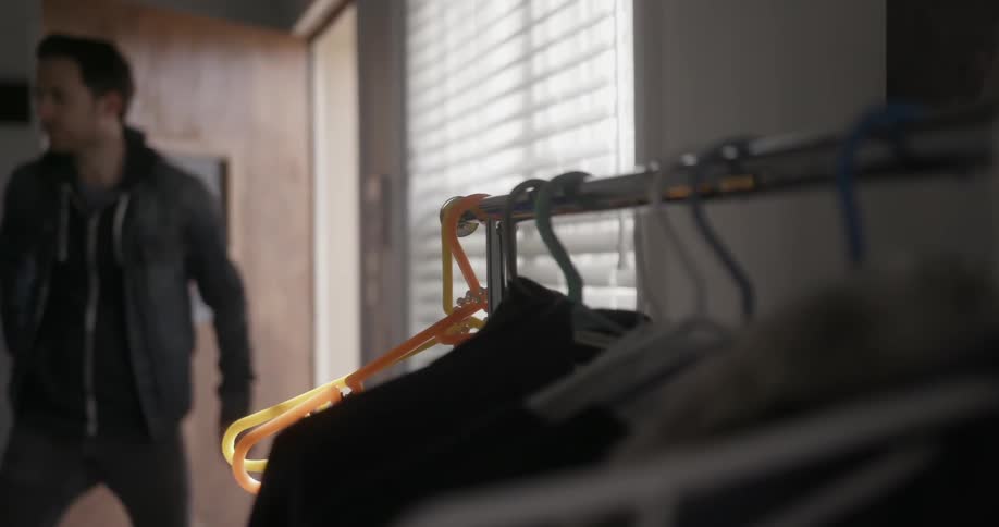 A man enters a room with clothes hanging on the side