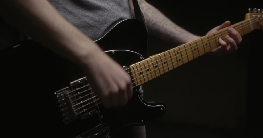 A man is standing in a studio and playing an electric guitar