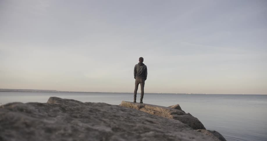 A man stands and stares off into a large body of water
