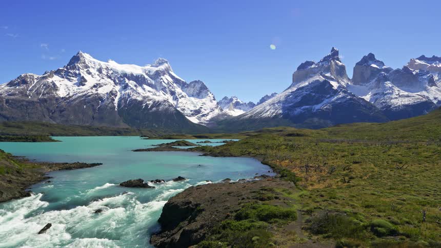 A landscape of turquoise waters flowing amidst rocky terrain with snowcapped mountains in the background