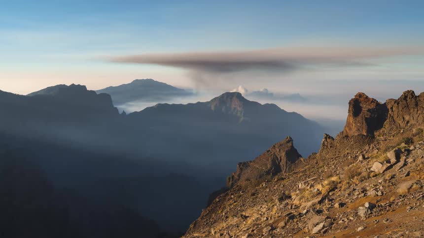 Volcanic smoke rising up to the sky in the distance beyond a mountain range