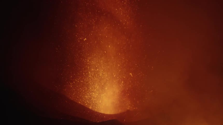 Volcano eruption at night with orange flames moving quickly and fountain of lava sparks surrounded by cloud of smoke