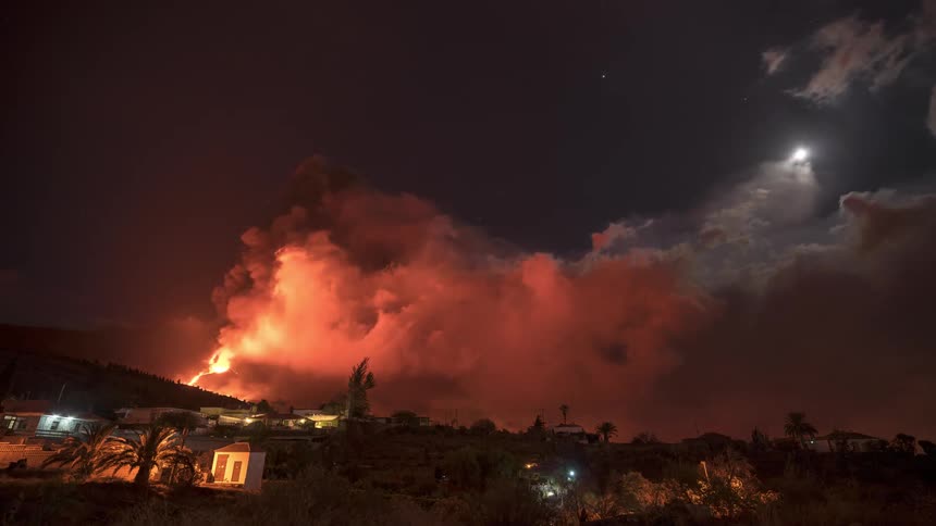 An erupting volcano releasing a lot of smoke near some houses