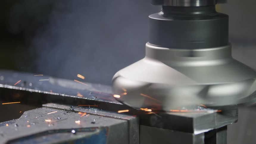 A machine with a circular head grinds a metal bar releasing sparks
