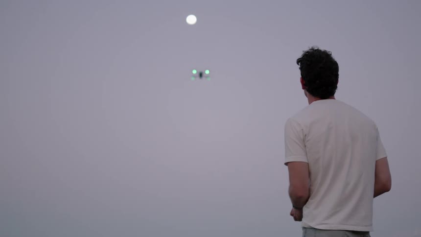A man flies a drone towards the moon at evening