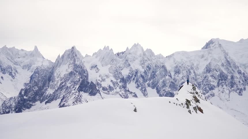 A person on top of a rock in a region with many snowcovered mountains