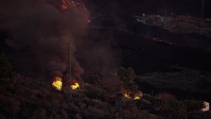 Flames rise from burning houses on a mountain side as a wildfire spreads
