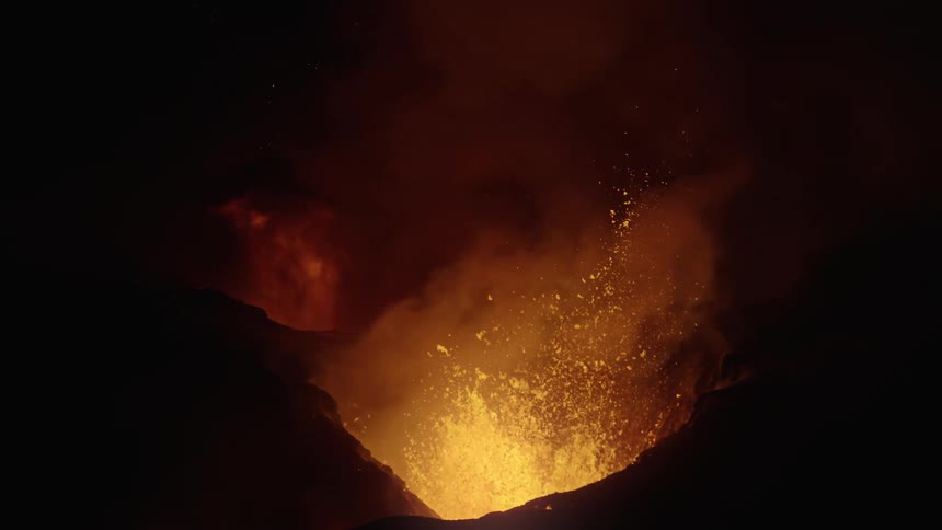 Hot magma glows as a volcano erupts and lava splashes as it flies into the air