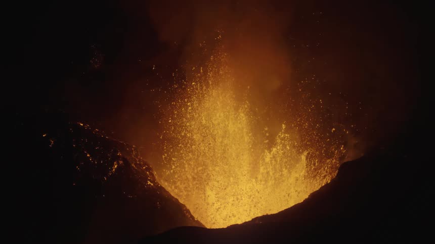 Volcano eruption at night with orange fountain of lava spewing up from mountain