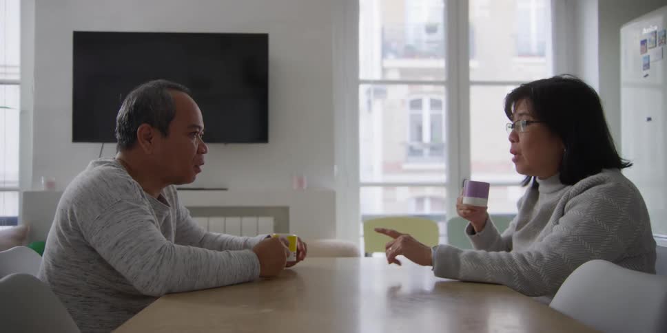 Couple sits at table in apartment and talks while drinking beverage from a cup