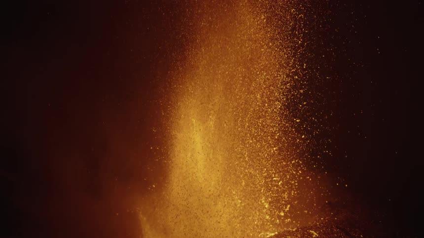 Lava sprays into the air from an erupting volcano as it glows in the darkness