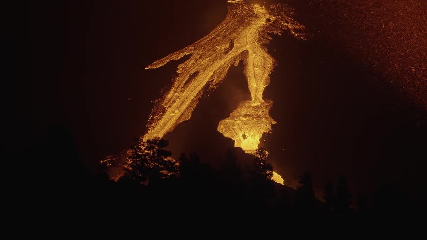 An erupting mountain volcano is releasing lava and it is falling onto the mountain