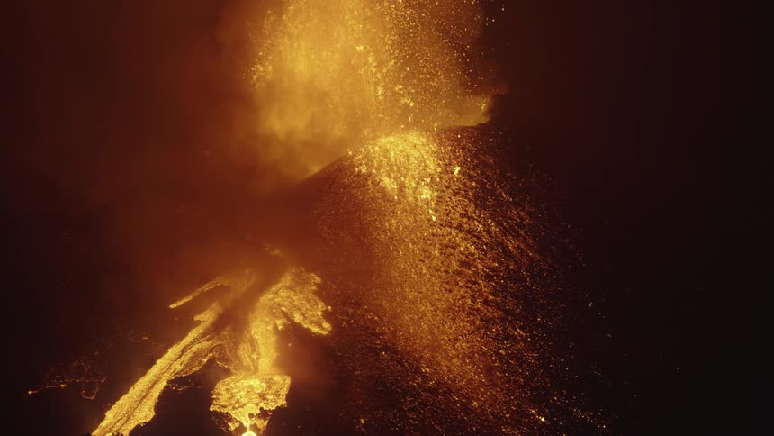 Aerial of an erupting volcanic crater with lava river on the mountain