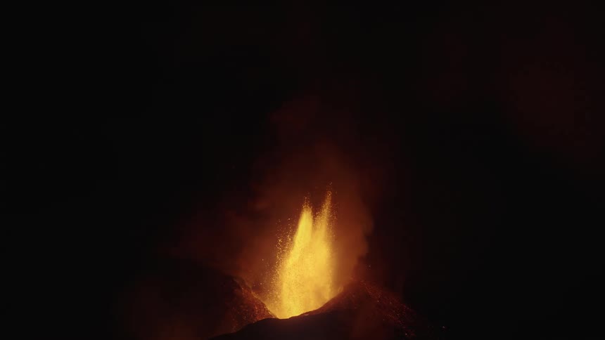 Slow motion volcanic eruption with fountain of orange flames shooting up from mountain at night